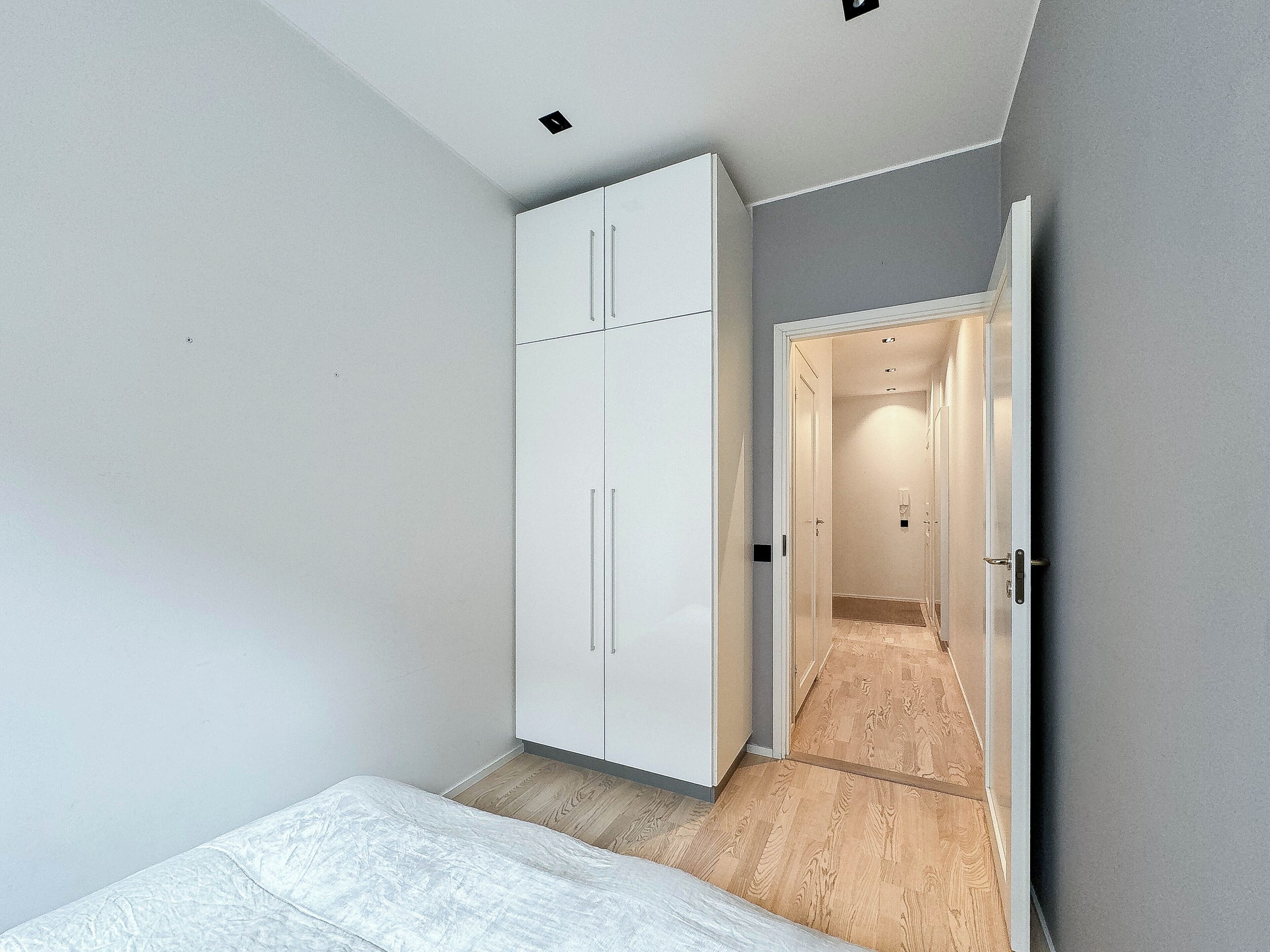 Camera da letto con un letto, un armadio bianco e un pavimento in legno.
