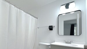Ein modernes Badezimmer mit Toilette, Duschvorhang, Waschtisch mit Spiegel und einer Leuchte darüber.