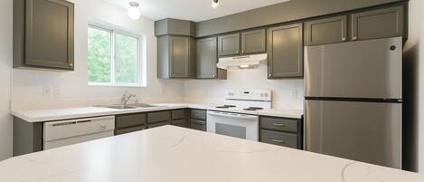 A modern kitchen with grey cabinets, a stainless steel refrigerator, a white stove, and a large island.