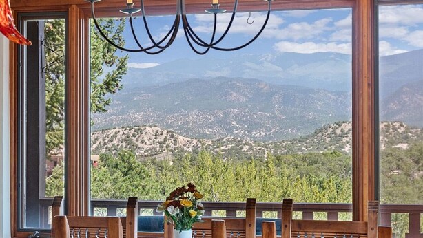 A dining area with a view of a mountainous landscape through large windows, a chandelier, and a table with a vase of flowers.