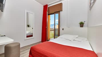 Ein modernes Hotelzimmer mit Bett, Schreibtisch, Spiegel und einem Balkon mit rotem Vorhang.