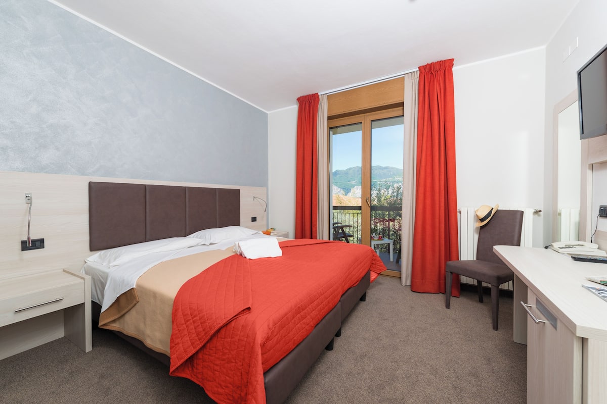 Quarto de hotel com cama, escrivaninha, cadeira e vista para o exterior.