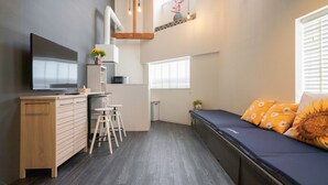 Un espacio habitable compacto con kitchenette, un sofá con cojines de girasol y un televisor sobre un mueble de madera.
