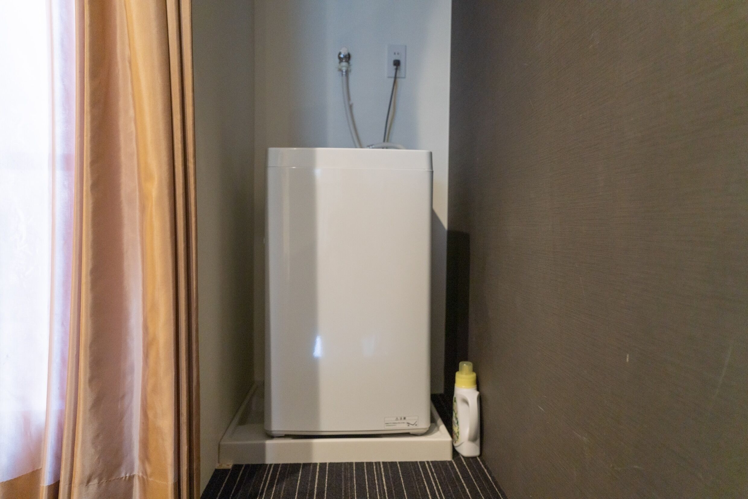 Ein weißer Kühlschrank steht in einer Ecke eines Raumes mit gestreiftem Boden.