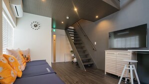 Una habitación moderna con sofá, una escalera, una zona de cocina y un reloj en la pared.