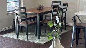 Un coin repas avec une table en bois, quatre chaises, un vase avec des fleurs, une carafe et une petite tasse.