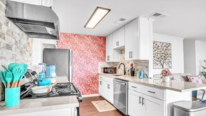 Une cuisine moderne avec des armoires blanches, une hotte de cuisinière en acier inoxydable et un pare-feu rouge à motifs floraux.