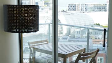 A balcony with a table and chairs, a lamp, and a view of buildings and mountains.