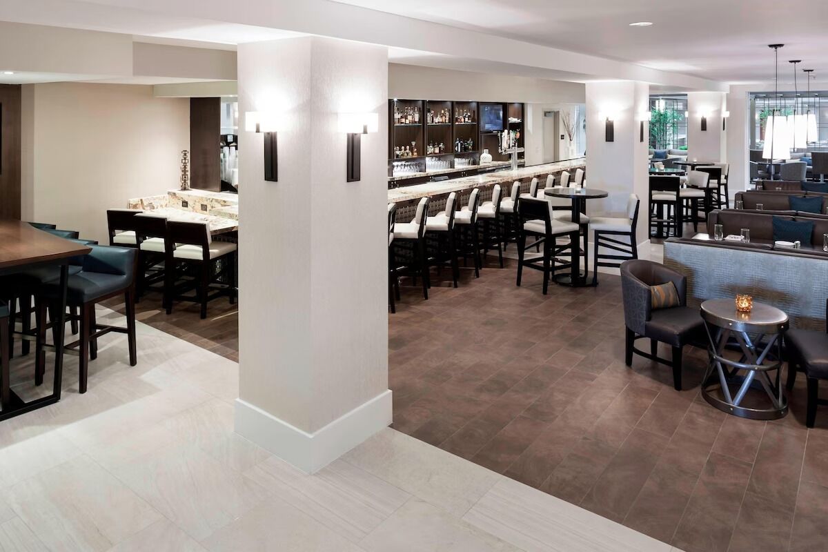 A modern hotel lobby with a bar area, seating arrangements, and a reception desk.