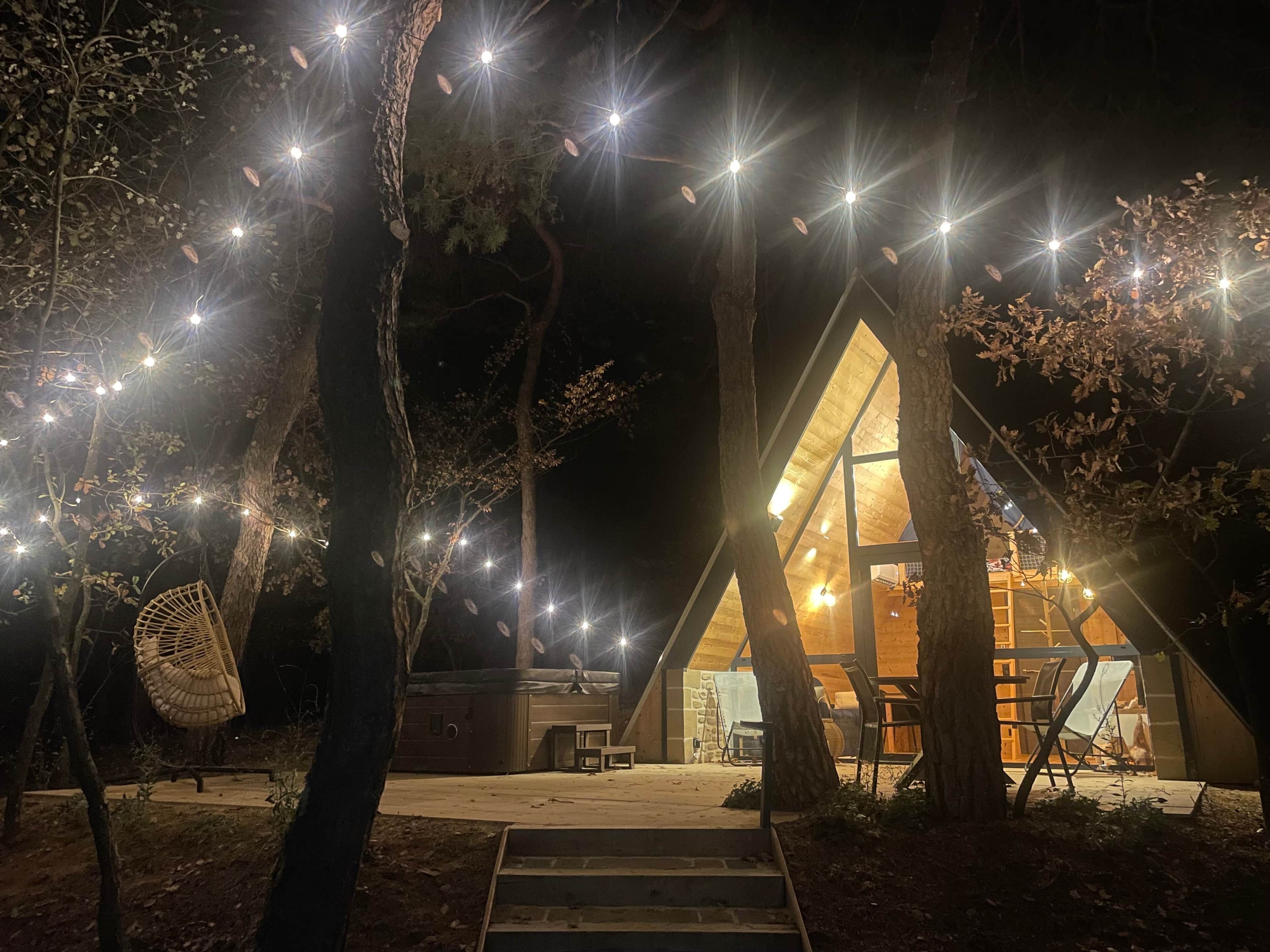 A cozy treehouse with a triangular roof, surrounded by trees and illuminated by string lights.