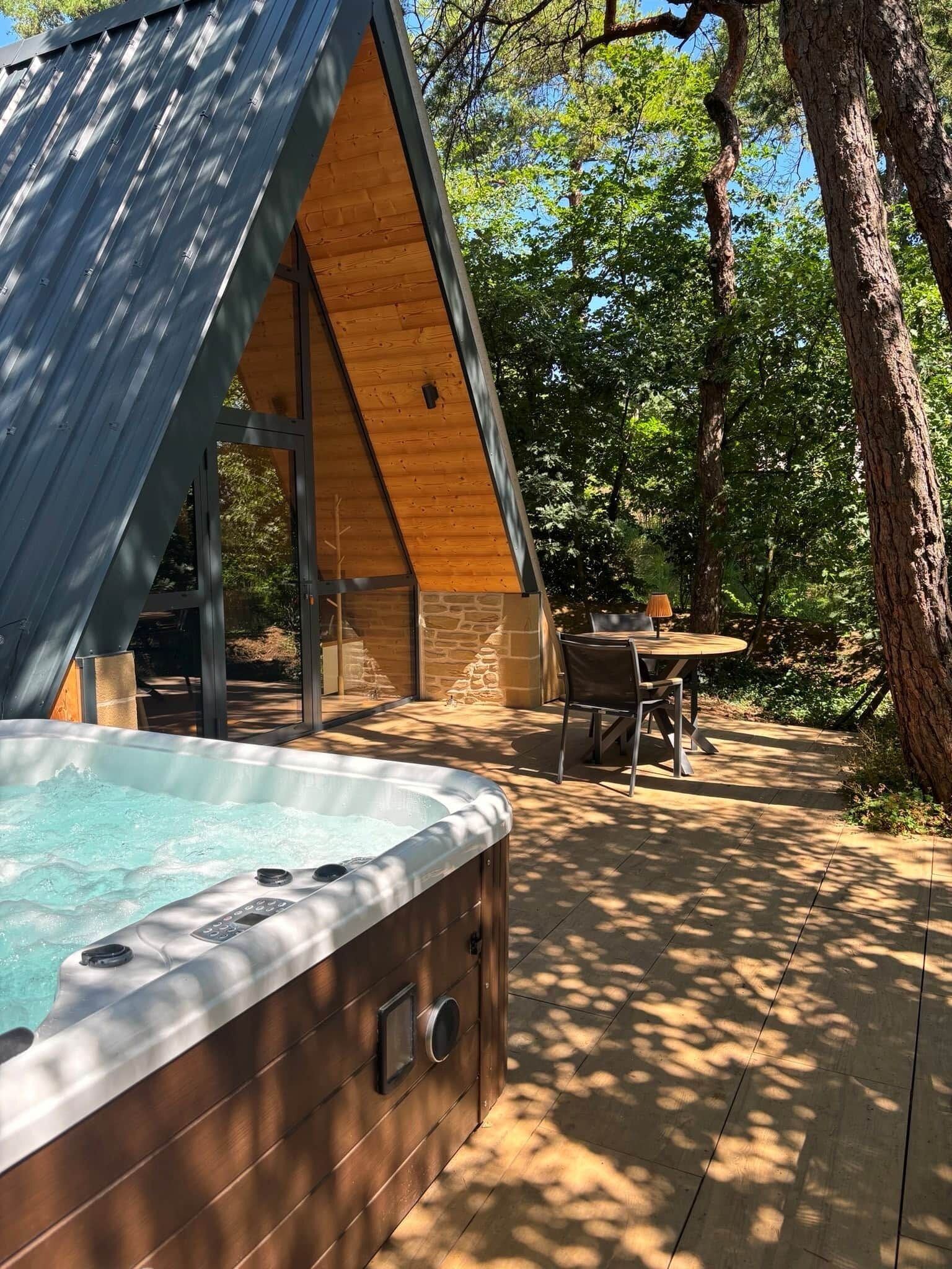 Un bain à remous dans un chalet en bois, avec un mur en pierre et une table avec des chaises à l’extérieur.