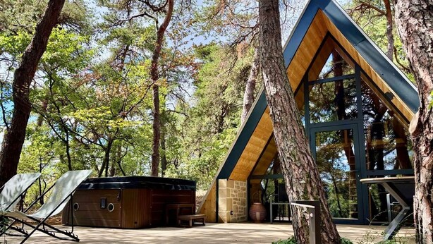 A cabin with a sloped roof, surrounded by trees, and a patio area with a chair and a hot tub. - CollinéA Chalet "CanopéA" 28 m² Private SPA (Bathernay)