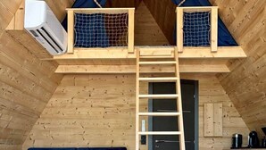 A loft-style room with a wooden interior, a blue sofa, a small round table with a vase of flowers, and a wooden ladder leading to a lofted sleeping area. - CollinéA Chalet "CanopéA" 28 m² Private SPA (Bathernay)