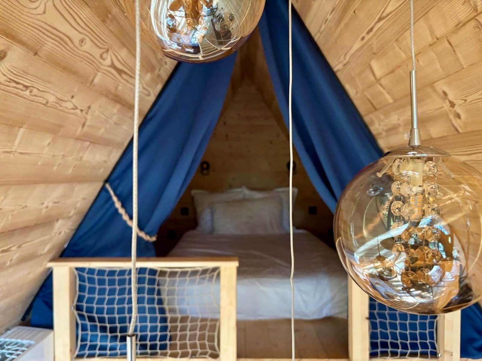A cozy tented room with a bed, blue curtains, and hanging glass lamps.