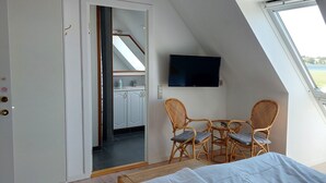 A bedroom with a bed, a TV, a dining table with chairs, and a view of a balcony with a window overlooking a body of water. - Rødkærgård Bed & Breakfast (Kerteminde)