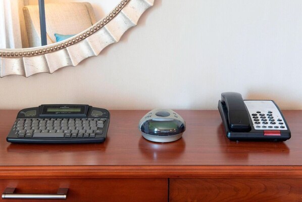 A wooden desk with a desktop computer, a digital camera, and a telephone.