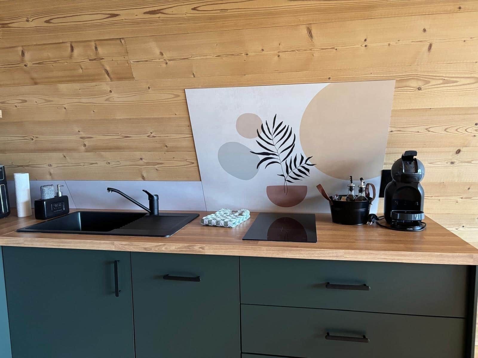 Een keuken met een houten aanrecht, een zwarte spoelbak, een koffiezetapparaat en een decoratief schilderij van een blad.