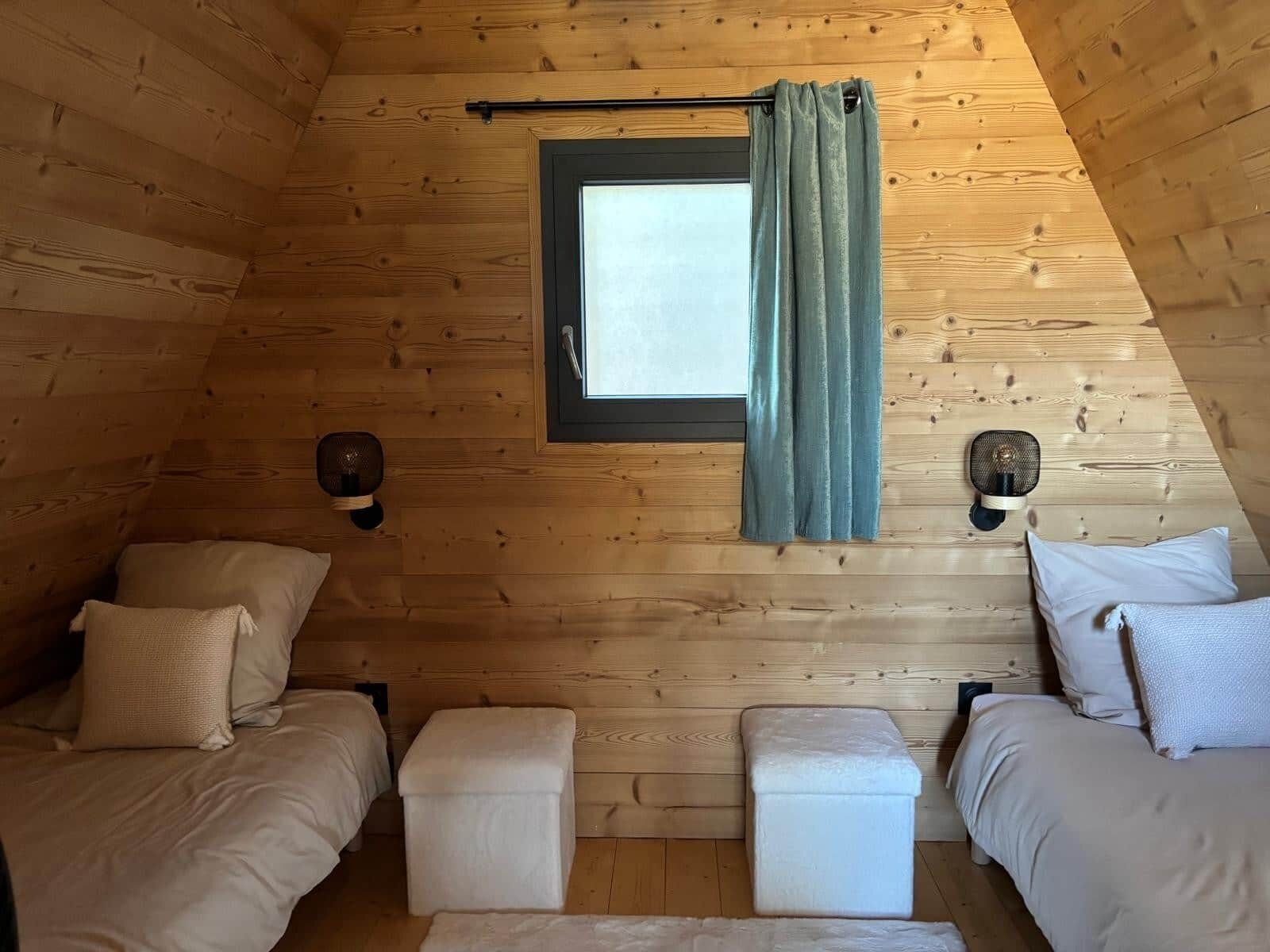 A cozy attic bedroom with two beds, a window with curtains, and wall-mounted lamps.