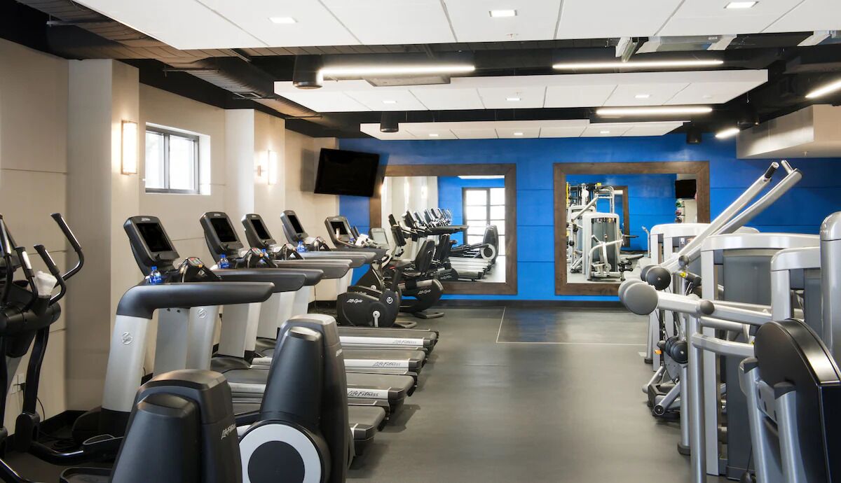 Une salle de sport équipée de plusieurs tapis de course, de plusieurs appareils de musculation elliptique et de matériel de musculation.