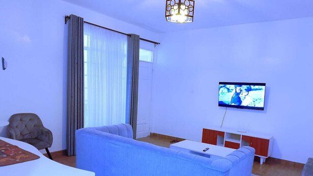 Un salon avec un canapé bleu, un téléviseur fixé au mur, une table blanche et un fauteuil marron.