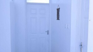 Un couloir avec une porte blanche au fond, une petite fenêtre au-dessus de la porte et un luminaire fixé au mur.