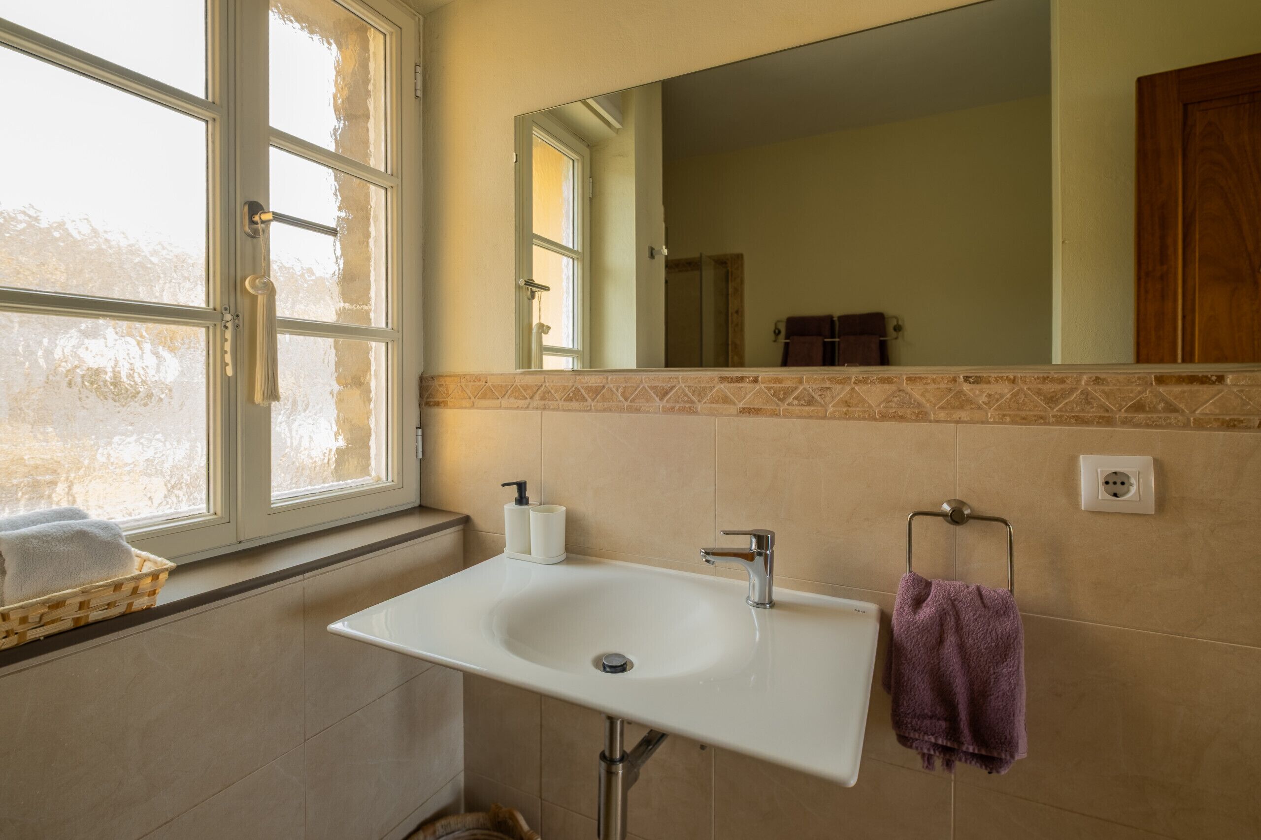 Ein Badezimmer mit einem weißen Waschbecken, einem Spiegel, einem Fenster und einem Handtuchhalter.