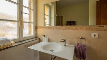 A bathroom with a white sink, a mirror, a window, and a towel rack.