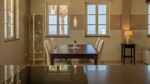 Ein Essbereich mit Tisch, Stühlen und einer Chandelüster. Es gibt eine Vitrine und eine Lampe auf einem Beistelltisch.