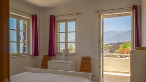 Ein Schlafzimmer mit Bett, Schreibtisch, Stuhl und Bergblick durch eine offene Tür.