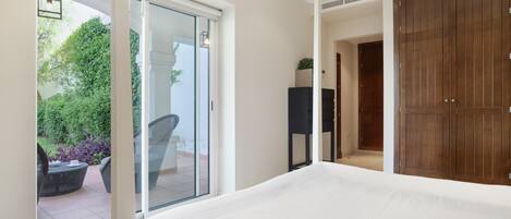 A bedroom with a large bed, a sliding glass door to a patio, and a wooden wardrobe.