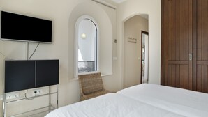 Een hotelkamer met een bed, een op een standaard gemonteerde televisie, een rieten stoel en een houten garderobe.