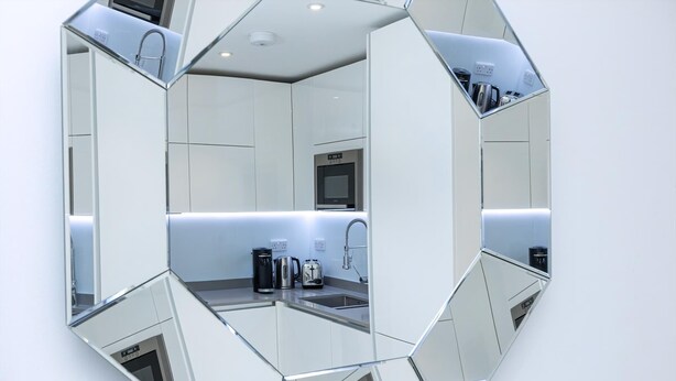 A hexagonal mirror reflecting a modern kitchen with a microwave, toaster, and coffee maker.