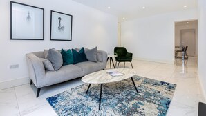 A modern living room with a grey sofa, a round coffee table, a blue patterned rug, and two framed pictures on the wall.