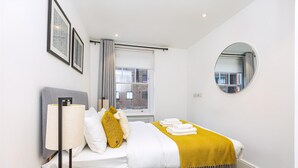 A modern bedroom with a bed, a bedside lamp, a mirror, and a window with curtains.
