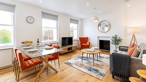 A modern living room with a dining area, large windows, a fireplace, and a television.