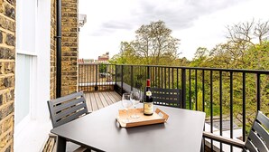 A balcony with a table, two chairs, a wine bottle, and glasses on a tray.