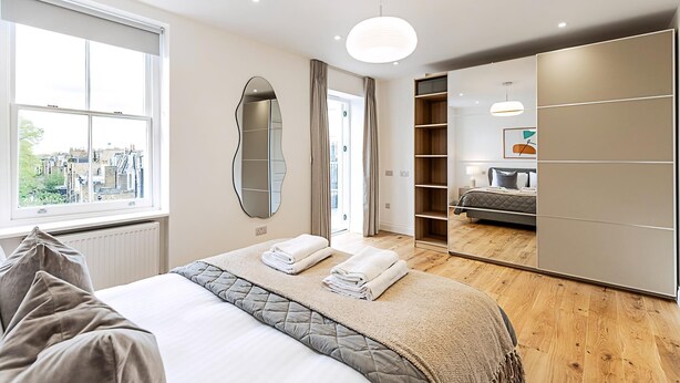 A modern bedroom with a large bed, a walk-in closet, and a view of the city through the window.