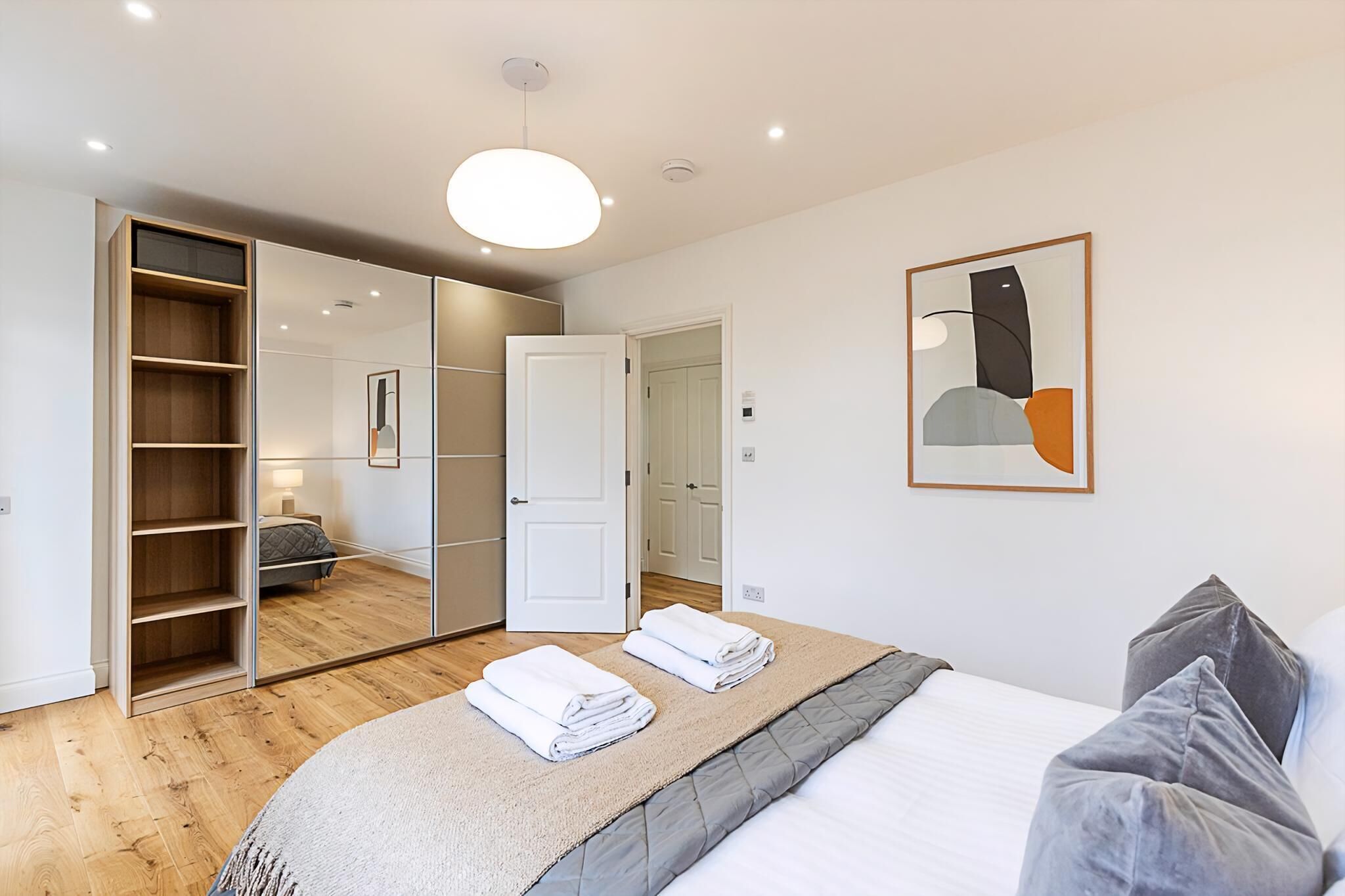 A modern bedroom with a large bed, a wardrobe, and a mirror.