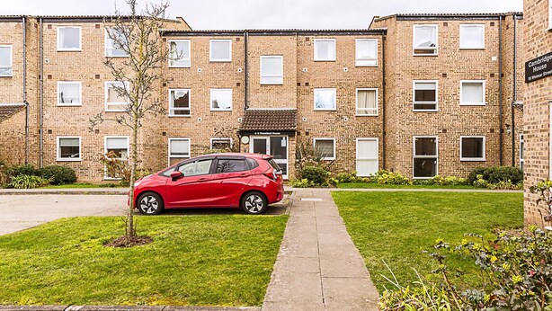 A red car parked in front of a brick apartment building with multiple windows and a small tree in the front yard. - Bright 2-bed Home Near Putney Riverside (London)