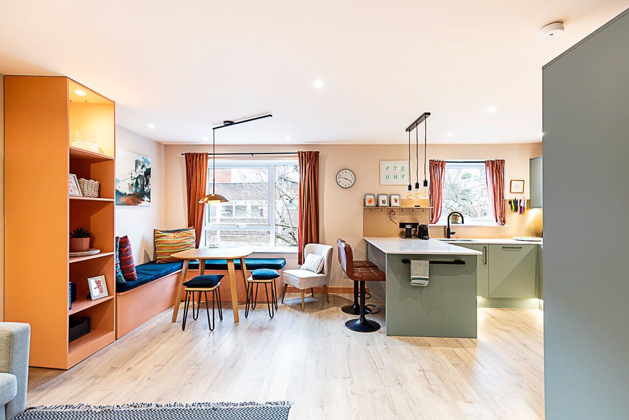 A modern kitchen with a dining area, a built-in bookshelf, and a large window with curtains.