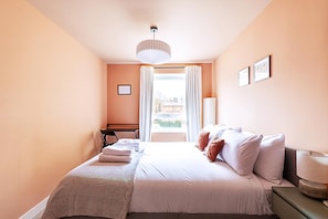 A bedroom with a bed, a desk, a chair, a lamp, and a window with curtains.