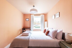 A bedroom with a bed, a desk, a chair, a lamp, and a window with curtains.