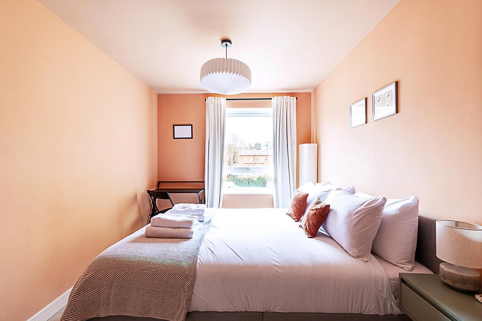Quarto com cama, escrivaninha, cadeira, luminária e janela com cortinas.