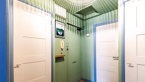 A hallway with two white doors, a green wall, a framed map, a small shelf, and a doormat. - Bright 2-bed Home Near Putney Riverside (London)