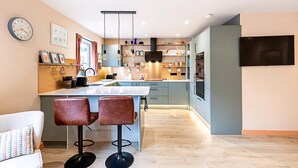 A modern kitchen with a central island, pendant lights, and a flat-screen TV. - Bright 2-bed Home Near Putney Riverside (London)
