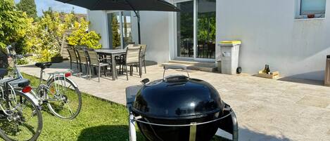 A patio with a grill, a bicycle, and a dining area with chairs and a table.