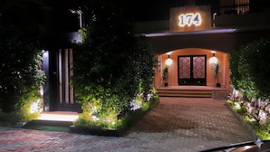 A hotel entrance with a brick pathway leading to a double door with a decorative pattern. There are potted plants on either side of the entrance and a sign above the door displaying the number 174. - Hotel Apartment in Sheikh Zayed – Zayed Suites A (First 6th of October)