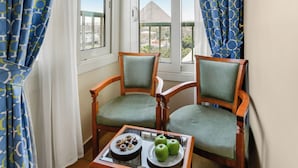 Un balcon avec deux chaises en bois, une table en verre sur laquelle sont disposées des pâtisseries et des pommes, et une vue sur une pyramide.