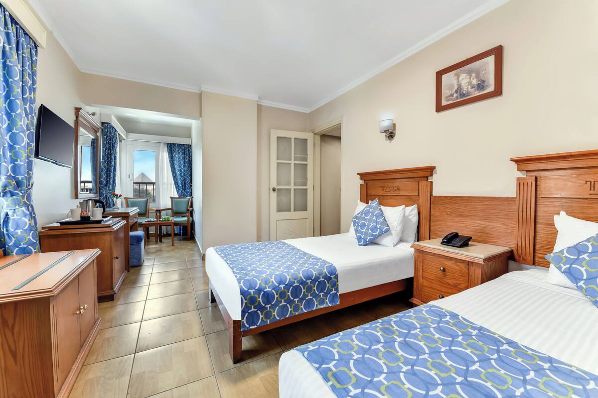 A hotel room with two beds, a desk, a chair, a TV, and a door leading to a balcony.