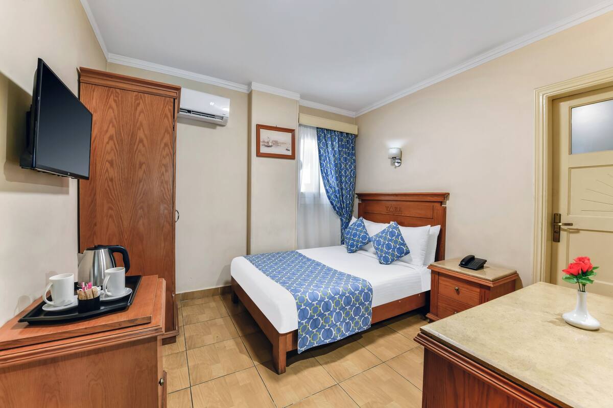 A hotel room with a bed, bedside table, TV, wardrobe, and a small desk with a tray of breakfast items.